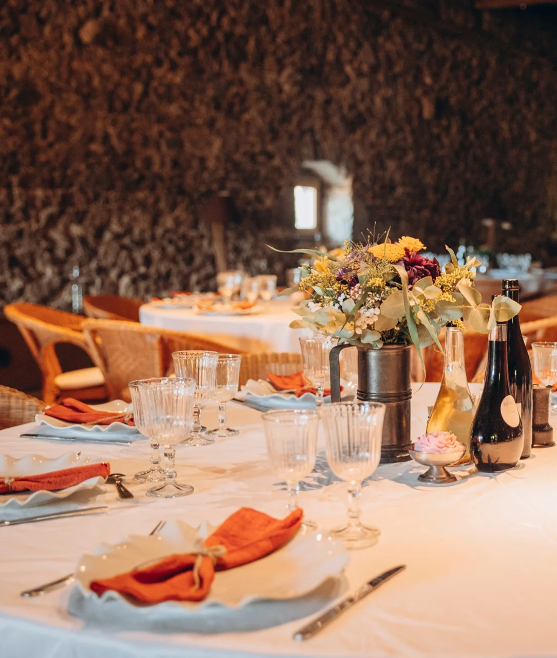 Table dressée avec verres, serviettes et bouquet de fleurs dans une salle aux murs de pierre